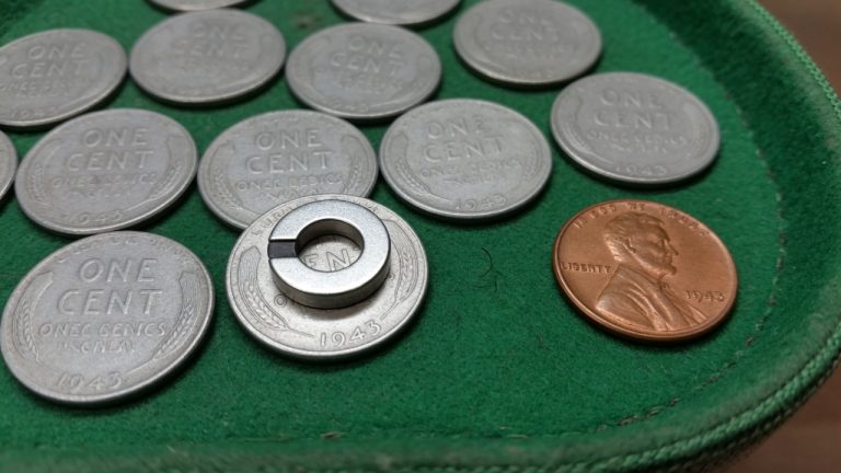 Gray 1943 steel cents on a green tray with a ring magnet on one coin and a copper Lincoln for color
