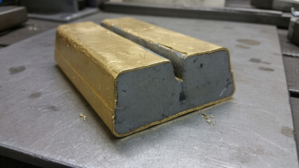 A gold-plated bar cut open to show a dull gray tungsten-like core