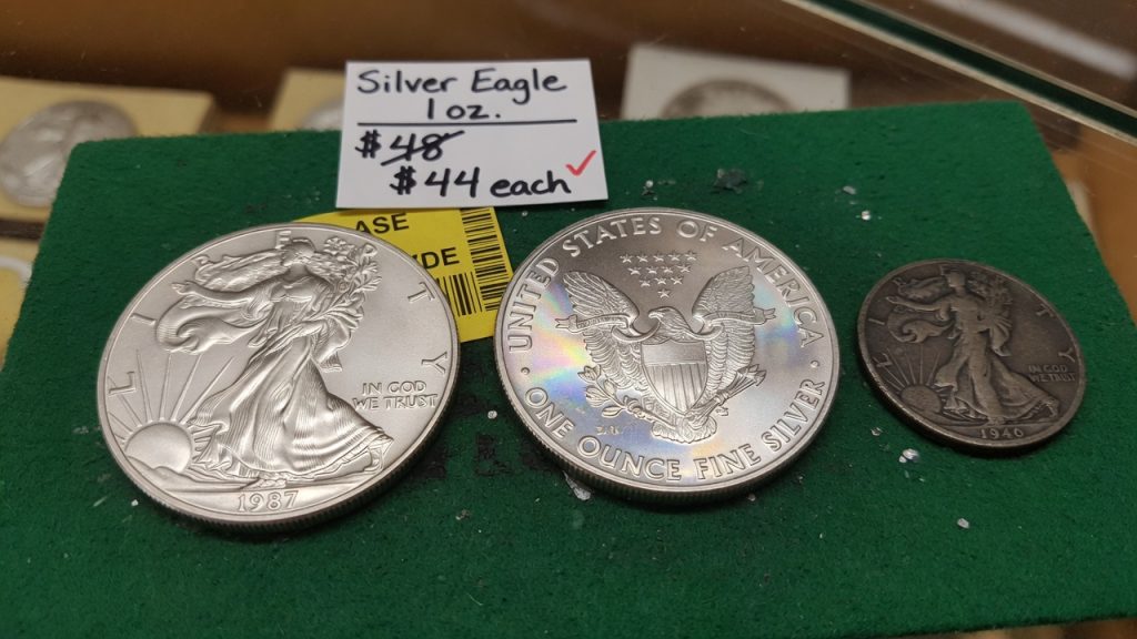 A 1987 Silver Eagle and reverse beside a smaller 1940 Walking Liberty half