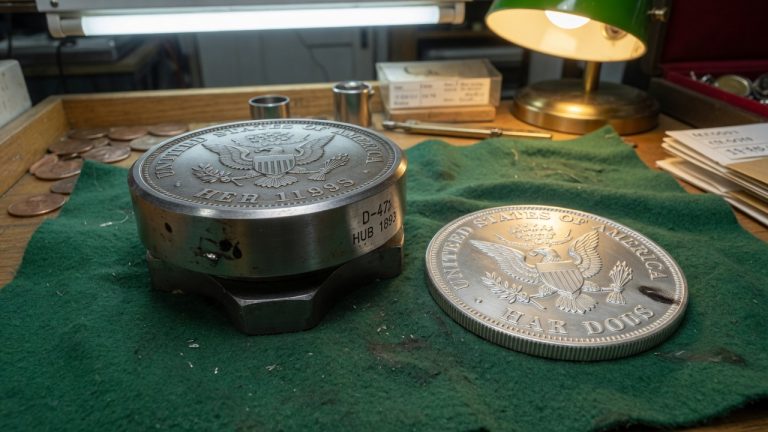 A steel coin die and a silver planchet on a green felt shop tray