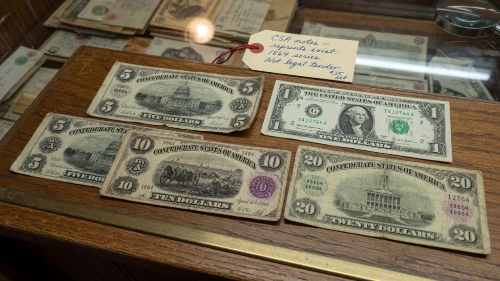 1864 Confederate $5, $10, and $20 notes on a wooden counter next to a modern US one-dollar bill