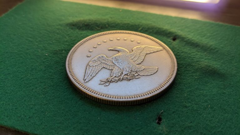 A seated Liberty silver dollar with a flying eagle reverse on green felt
