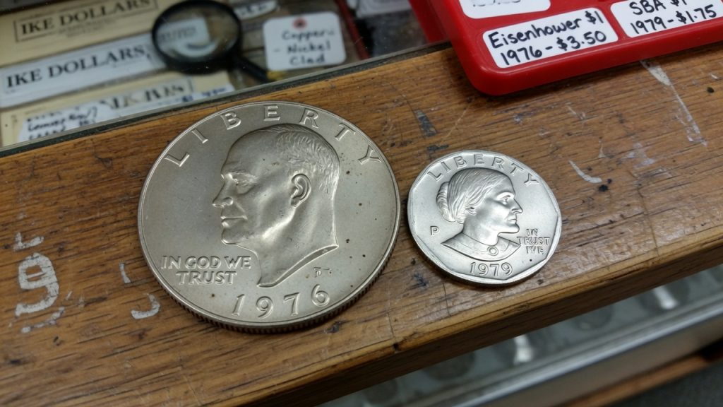 A 1976 Eisenhower dollar next to a smaller 1979 Susan B. Anthony dollar on a wooden counter