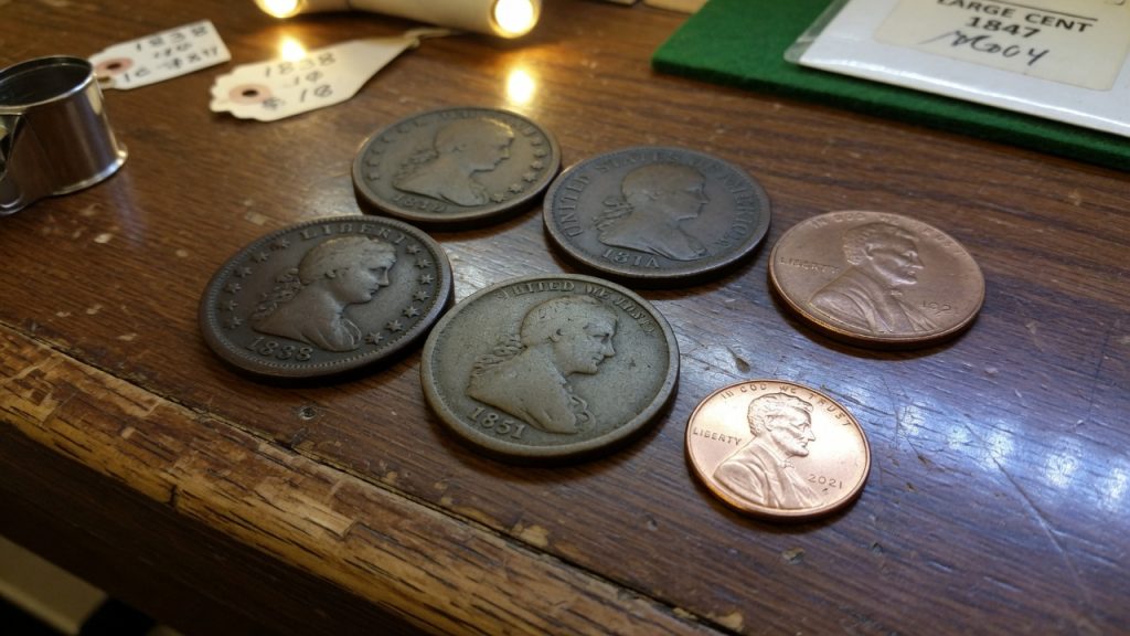 Four worn large cents on a wooden counter next to two small Lincoln cents for size