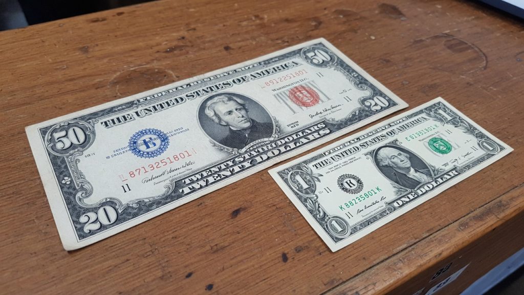 A large-size United States note next to a modern small-size bill on a wooden counter