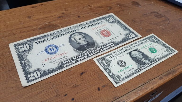 A large-size United States note next to a modern small-size bill on a wooden counter