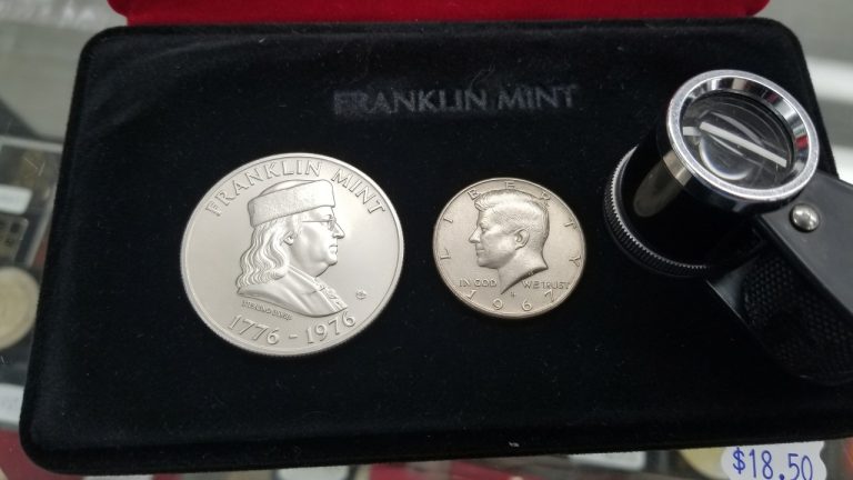 A Franklin Mint sterling medal in a case next to a Kennedy half dollar and a loupe