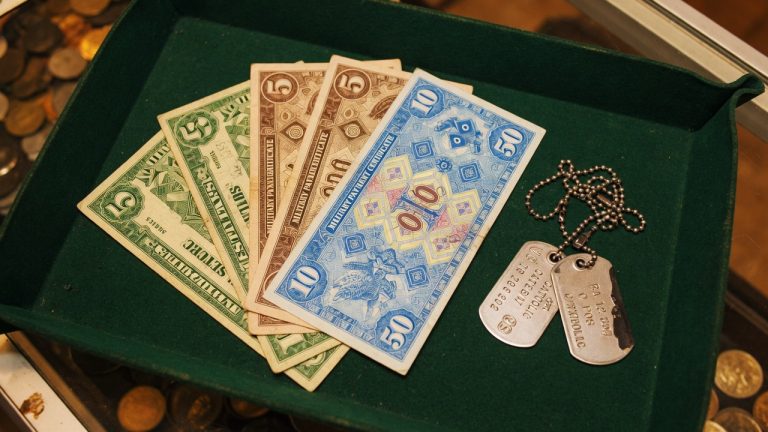 Colorful military payment certificates fanned on a green tray beside dog tags