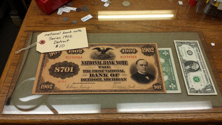 A Series 1902 national bank note from Detroit beside a modern one-dollar bill