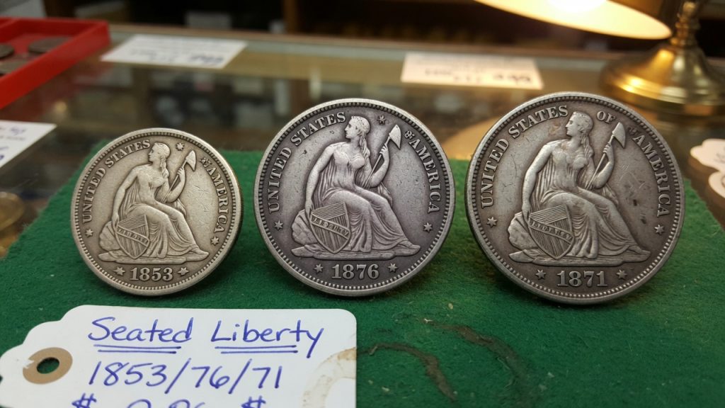 Three Seated Liberty silver coins dated 1853, 1876, and 1871 on green felt