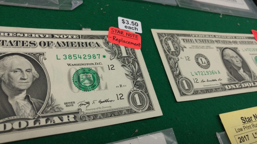 A one-dollar Federal Reserve note with a star at the end of the serial number next to a regular note