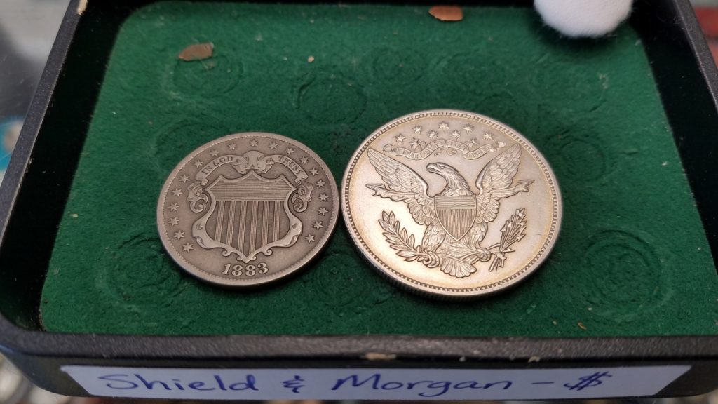 A Shield nickel and a heraldic-eagle reverse silver dollar on green felt