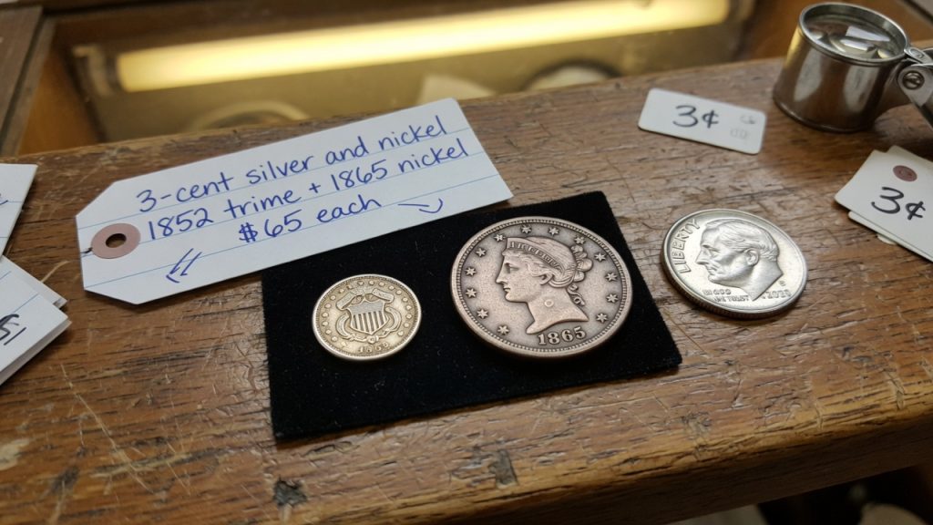 A tiny silver three-cent piece beside a copper-nickel three-cent nickel