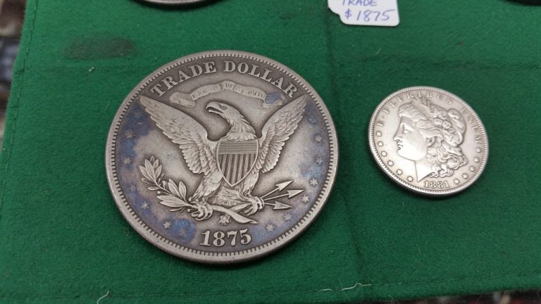 An 1875 Trade dollar reverse beside a smaller Morgan dollar on green felt