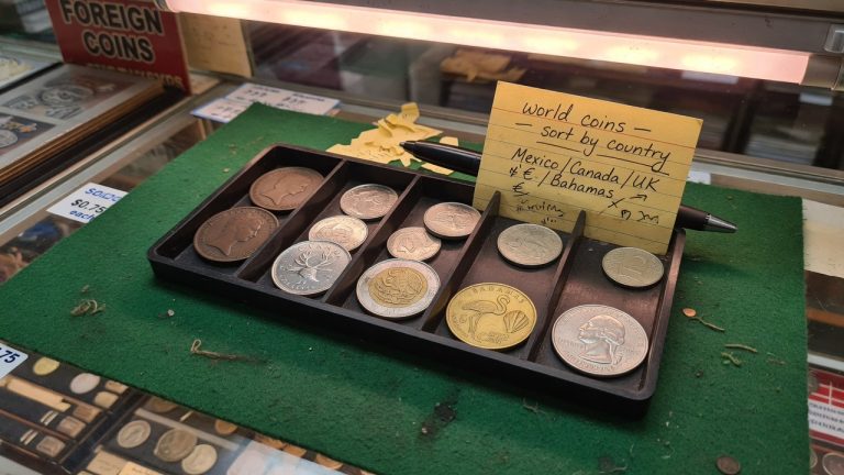 A shop tray of world coins — UK pennies, Mexico, Bahamas flamingo, and a US quarter — tagged sort by country